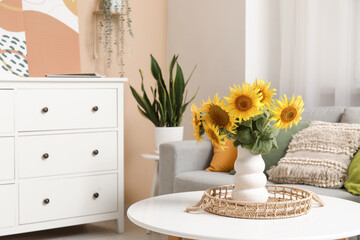 Wicker tray and vase with beautiful sunflowers on table in interior of living room