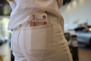 In the image, a woman is holding money in her back pocket with a car in the background