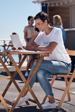 Smile, phone call and woman with laptop, outdoor and restaurant in morning for scriptwriter with sunglasses. Summer, listening and happy with computer and paper for inspiration, web and creative
