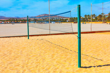  Beach volleyball net set up on sandy shore. Volleyball net is green and is attached to a metal pole, beach is empty, with no people 
