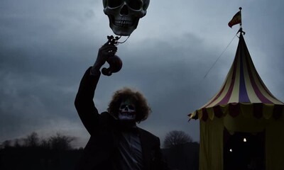 A man in a clown costume holding a skull mask. The image has a creepy and eerie mood 4K Video