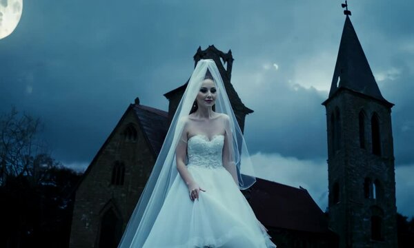 Halloween ghost bride with a flowing veil, standing in front of an old, abandoned church. Video