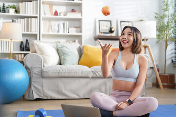 young sporty woman in sportswear sitting on yoga mat in the living room,throw up an apple during fitness training,concept of people lifestyle,workout,health care