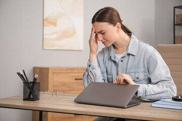 Embarrassed woman at wooden table with laptop in office