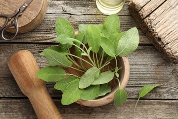 Fresh sage leaves, mortar, pestle and scissors on wooden table, flat lay