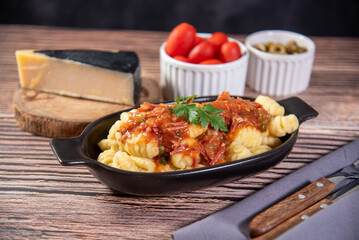 Gnocchi with parmesan cheese on the side in tomato sauce on a wooden table with preparation components around it