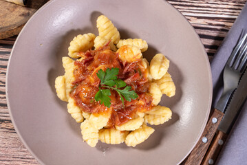 Gnocchi with parmesan cheese on the side in tomato sauce on a wooden table with preparation components around it