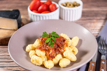 Gnocchi with parmesan cheese on the side in tomato sauce on a wooden table with preparation components around it