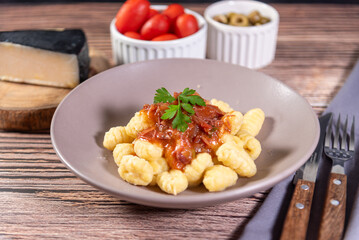 Gnocchi with parmesan cheese on the side in tomato sauce on a wooden table with preparation components around it