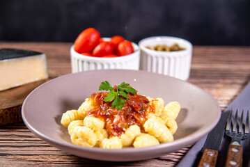 Gnocchi with grated parmesan cheese in tomato sauce on a wooden table with preparation components around it