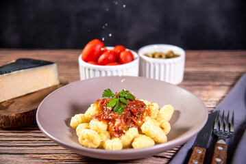 Gnocchi with grated parmesan cheese in tomato sauce on a wooden table with preparation components around it