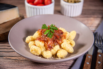 Gnocchi with grated parmesan cheese in tomato sauce on a wooden table with preparation components around it