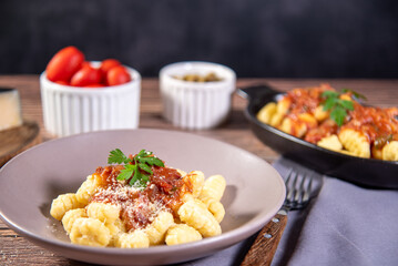 Gnocchi with grated parmesan cheese in tomato sauce on a wooden table with preparation components around it