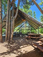 Large outdoor firepit and dining area with large wooden tables and covered with a large canvas tent