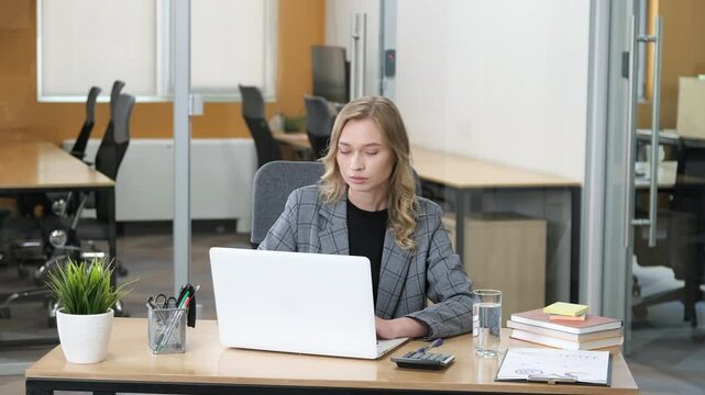 A businesswoman wearing a gray plaid blazer over a black top, embodying professional attire. Professional woman busy working using her laptop and thinking ideas while touching her chin.