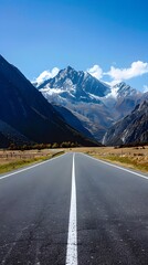 Fototapeta premium Smooth asphalt road with majestic mountain peaks and clear blue sky
