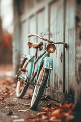 Obraz premium A blue bicycle is leaning against a wooden wall. The bike is old and has a vintage look to it. The leaves on the ground around the bike give it a rustic feel