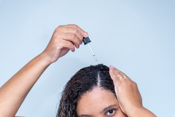 Fototapeta premium Woman applying essential oil to hair roots on gray background, closeup