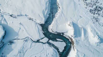 A bird's-eye view of a snowy landscape, with a river cutting through the white expanse. The contrast between the snow and the flowing water creates a striking and serene winter scene.