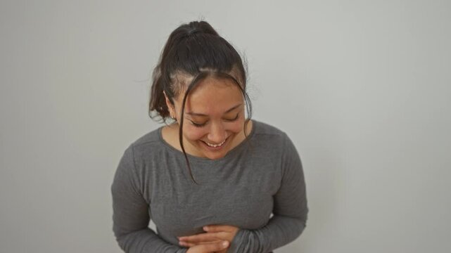 Bursting out laughing, a young hispanic woman standing over white isolated background, chuckling hard at a funny joke, smiling faces radiating joy and positivity