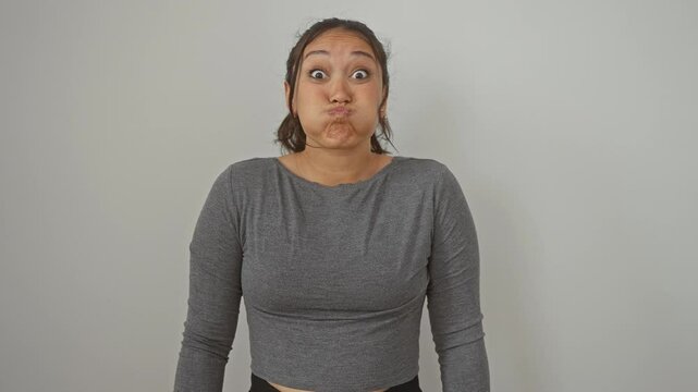 Hilarious portrait of young, beautiful hispanic woman having a goofy moment. standing, with cheeks puffed full of air, catching breath over isolated white background.