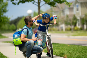 Naklejka premium Father and son riding bike in park. Child in safety helmet with father riding bike in summer day. Father teaching son riding bike. Fatherhood. Support parent. Fathers day. Child care. Fathers day.