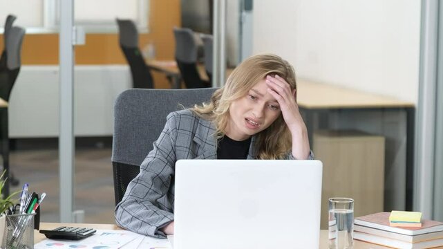 Professional working on her laptop remove having a problematic face. A woman having trouble at work, massaging her head with two hands.