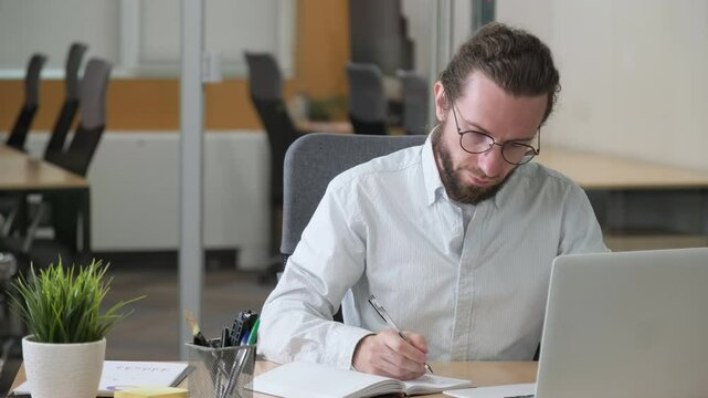 An office man concentrate working on his desk. Businessman looking at the screen and writing in notebook. Planning.