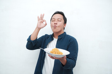 A portrait of happy Asian man wearing a blue shirt excited to eat a plate of fried noodles. Young man smiling and holding a plate of noodle. Isolated with a white background.