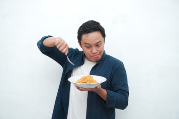 A portrait of happy Asian man wearing a blue shirt excited to eat a plate of fried noodles. Young man smiling and holding a plate of noodle. Isolated with a white background.