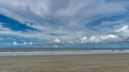 Beautiful sea and sky scenery. Turquoise ocean waves foam and spread over the sandy beach. Picturesque cumulus and cirrus clouds in the blue sky. Malaysia. Borneo. Kota Kinabalu