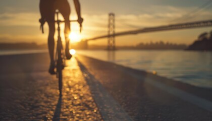 Silhouette of cyclist riding towards sunrise with bridge in background.