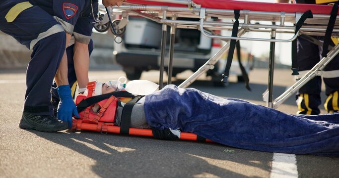 Person, accident and emergency on street with stretcher for support, medical response to trauma with oxygen. Safety, first aid or health insurance or air mask for breath on road, ems or crisis - Powered by Adobe