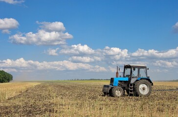 Obraz premium blue tractor in the field during the harvest season. rural landscape with field and tractor