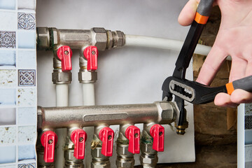 Repairing water pipe manifold in country house, plumber uses adjustable pliers to unscrew elbow...