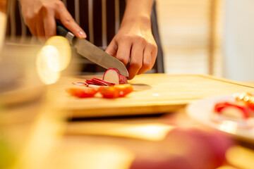 Happy Asian woman enjoy indoor healthy lifestyle cooking and having dinner at home. Attractive girl preparing food and cut radish on cutting board for making vegetables salad in the kitchen.