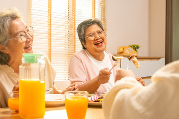 Group of Happy Asian senior women having dinner together at home. Elderly retired woman friends enjoy indoor lifestyle meeting party eating healthy food and vegetables salad together on dining table.