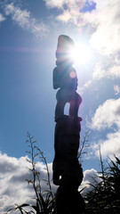 Sunlight behind Maori pou carved wooden statue overlooking the capital city of Wellington, New...