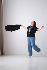 businesswoman enjoys a playful moment, tossing her blazer while wearing a black top, blue jeans,...