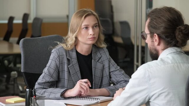 Two business professional having a serious discussion. A woman listen and take notes in front of her workmate. Office workers having a one-on-one meeting in a modern office.