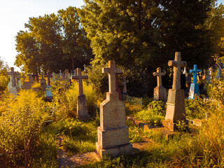 Old cemetery on a sunny morning. Stone crosses, burial places. Graves overgrown with grass.