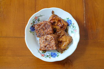 Tempeh and Tahu Bacem in white plate on the wood table, traditional Indonesian dishes with a sweet taste.