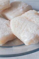 Frozen haddock fillets defrosting on a glass plate. On a light grey granite background