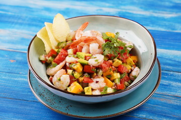 Ceviche salad with shrimps, mango and avocado in a plate on blue background. Latin American food. Delicious, freshly made shrimp ceviche. Shrimp marinated in lime and orange .