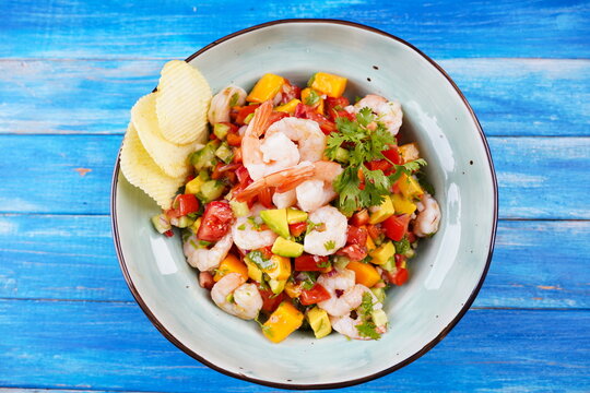 Ceviche salad with shrimps, mango and avocado in a plate on blue background. Latin American food. Delicious, freshly made shrimp ceviche. Shrimp marinated in lime and orange .