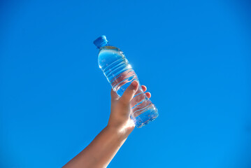 A girl holds a bottle of drinking water in her hand against a blue sky background
