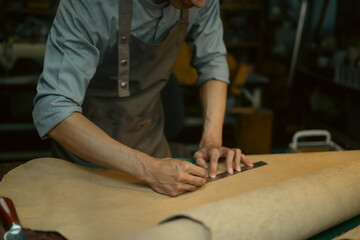 Male artisan is meticulously measuring and cutting a large piece of leather on workbench