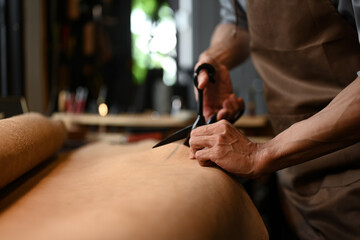 A craftsman working diligently, cutting leather in his workshop with various tools.