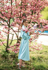 Caucasian woman in blue dress stands by pink magnolia tree