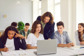 Teacher providing assistance to teenage students during a lesson in a school classroom. Supportive learning environment where pupils are engaged and receiving guidance from teacher.